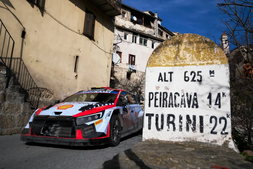 Coche de rally cerca de señal de dirección en pueblo.