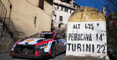 Coche de rally cerca de señal de dirección en pueblo.