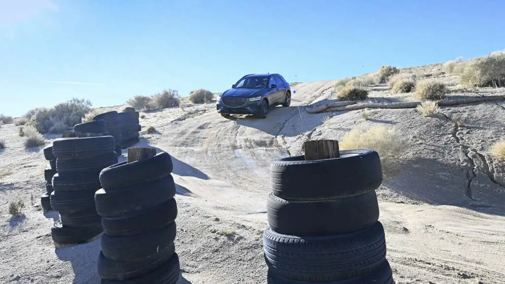 Coche maniobrando en terreno rugoso cerca de pilas de neumáticos.