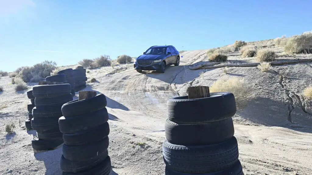 Un coche cruzando un terreno árido con pilas de neumáticos usados.