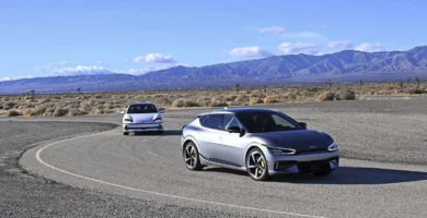 Dos coches modernos en una carretera desértica con montañas al fondo.