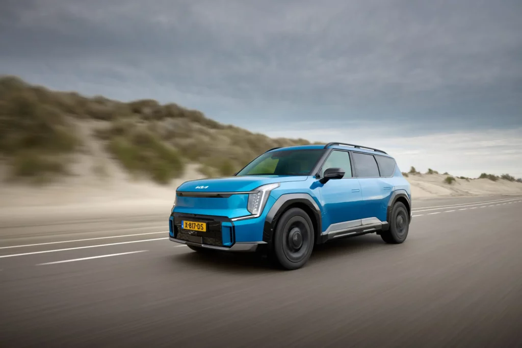 Coche azul eléctrico conduciendo rápido en carretera junto a dunas.