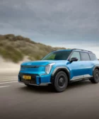 Coche azul eléctrico conduciendo rápido en carretera junto a dunas.