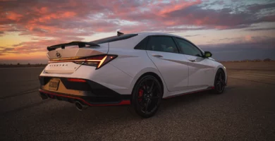 Auto deportivo blanco contra un atardecer nuboso vibrante.