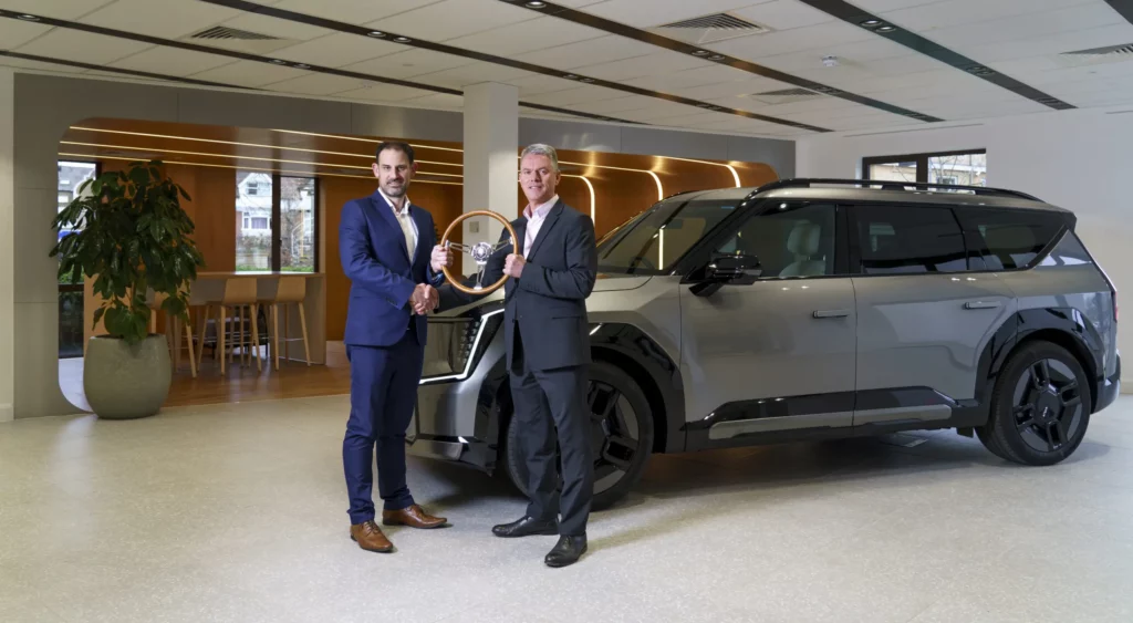 Dos hombres de negocios con un trofeo junto a un vehículo SUV.