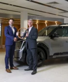 Dos hombres de negocios con un trofeo junto a un vehículo SUV.