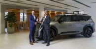 Dos hombres de negocios con un trofeo junto a un vehículo SUV.