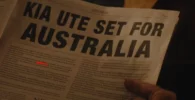 Persona sosteniendo periódico con anuncio "KIA UTE SET FOR AUSTRALIA".