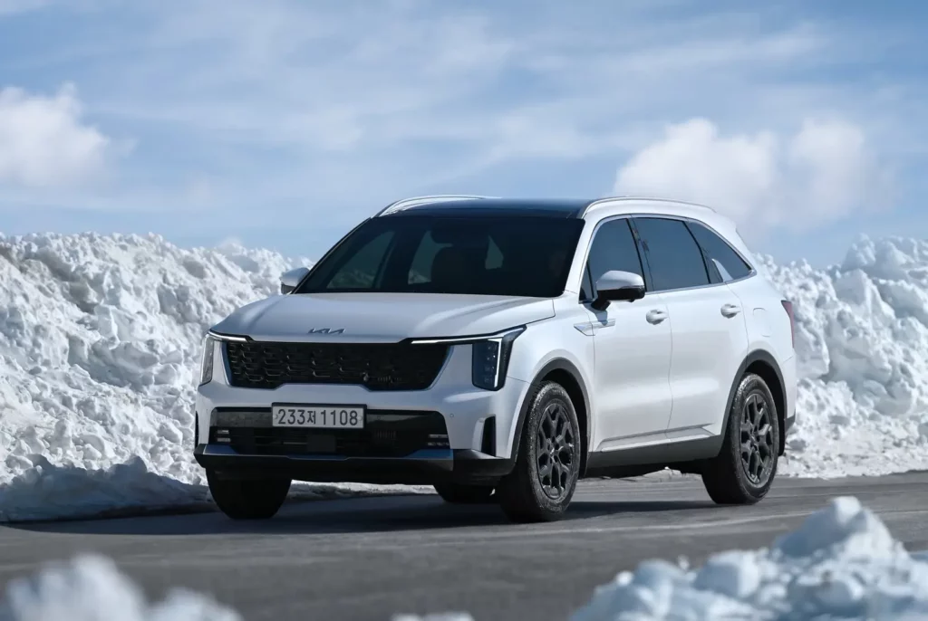 SUV blanco Kia aparcado frente a montañas de nieve.