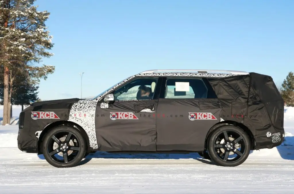 Vehículo camuflado en pruebas sobre nieve con árboles al fondo.