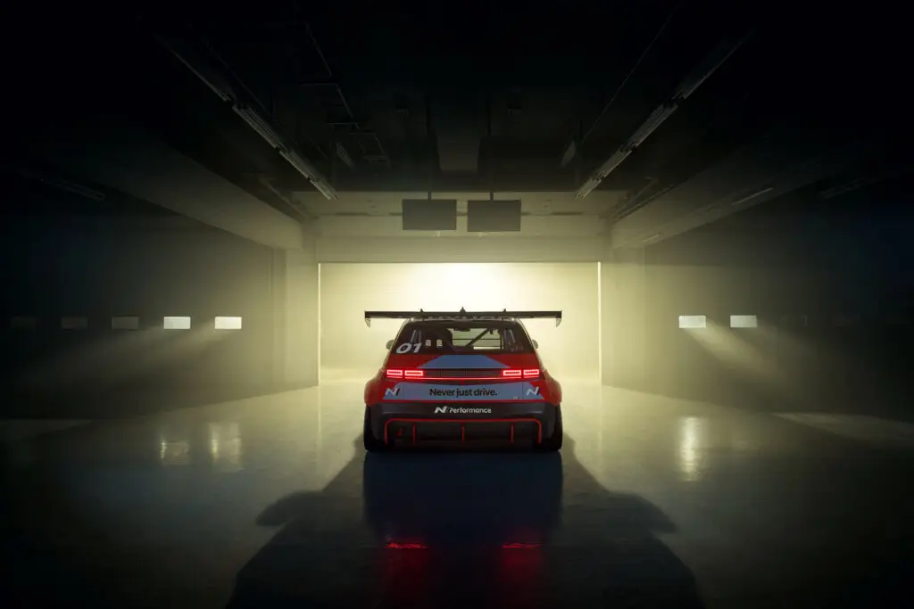 Auto de carreras rojo en un garaje iluminado por haces de luz.