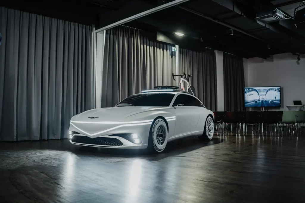 Automóvil futurista blanco en sala de exposiciones con bicicleta sobre él.