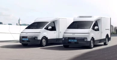 Dos furgonetas blancas estacionadas frente a una ciudad.