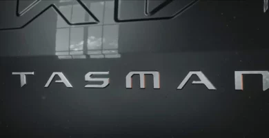 Logotipo metálico con la palabra "TASMAN" en un fondo oscuro.