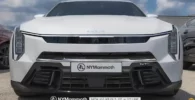 Automóvil blanco Kia con placa de marca destacada en el frente.