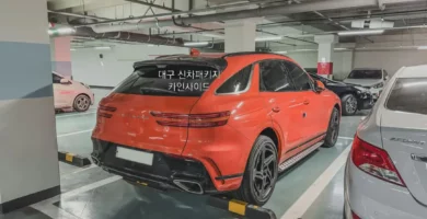 Camioneta Porsche Cayenne naranja estacionada en un parking subterráneo.