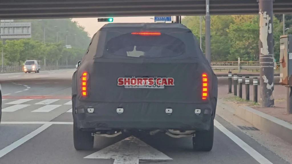 Un vehículo camuflado con luces traseras encendidas en una carretera.