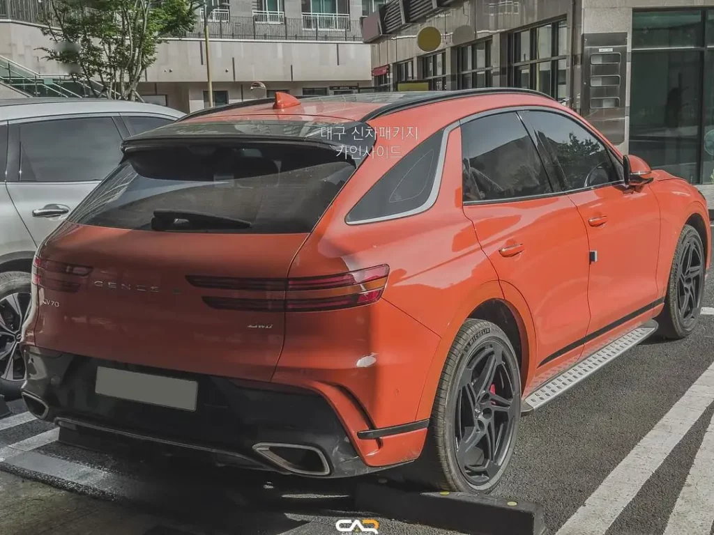 SUV naranja estacionada en la calle con edificios de fondo.