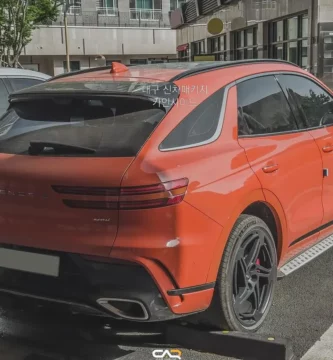 SUV naranja estacionada en la calle con edificios de fondo.