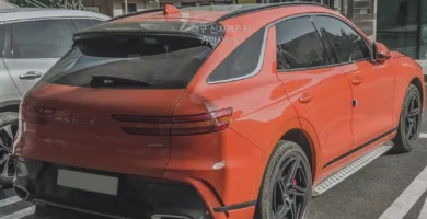 SUV naranja estacionada en la calle con edificios de fondo.