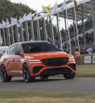 Coche naranja en exhibición, con espectadores y banderas de fondo.