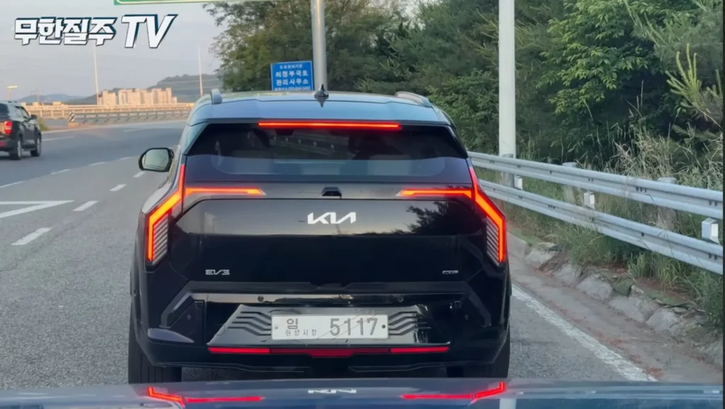 Vehículo negro en carretera con letrero y árboles alrededor.