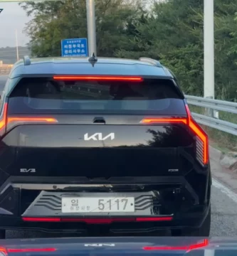 Vehículo negro en carretera con letrero y árboles alrededor.