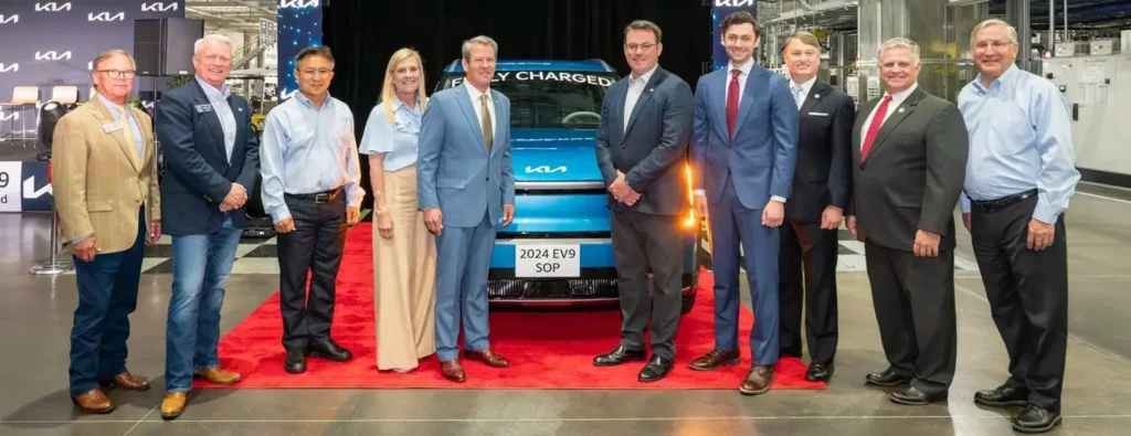 Grupo de personas posando frente a un auto eléctrico en una planta.