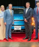 Grupo de personas posando frente a un auto eléctrico en una planta.