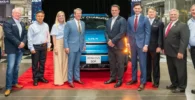 Grupo de personas posando frente a un auto eléctrico en una planta.