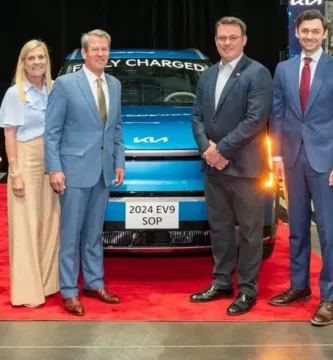 Grupo de personas posando frente a un auto eléctrico en una planta.