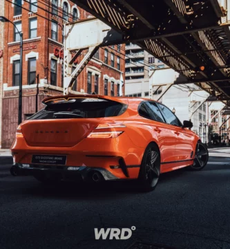 Coche naranja deportivo en un entorno urbano, bajo un puente elevado.