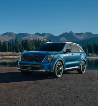 Coche azul junto a un lago, rodeado de montañas y árboles.