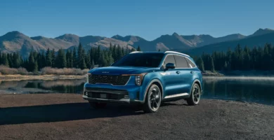 Coche azul junto a un lago, rodeado de montañas y árboles.