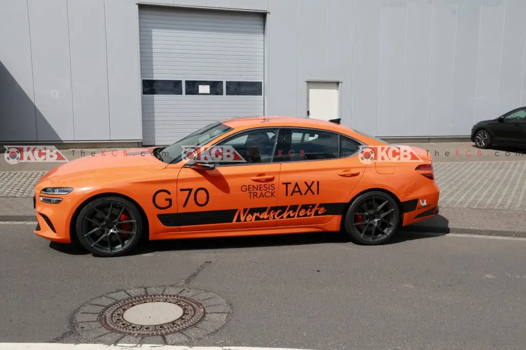 Coche naranja con publicidad, modelo G70, estacionado frente un edificio.