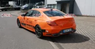 Coche deportivo naranja con publicidad en un entorno industrial.