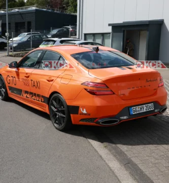 Coche deportivo naranja con publicidad en un entorno industrial.