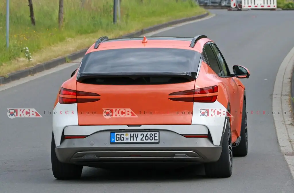 Coche naranja y blanco en una carretera, visto desde atrás.