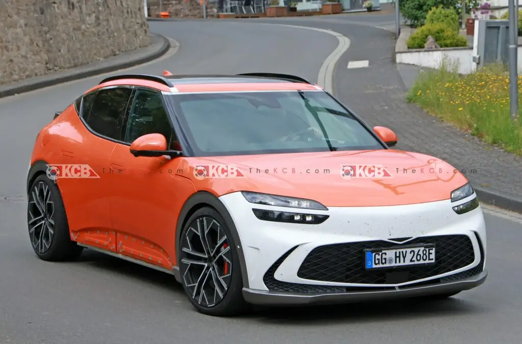 Coche eléctrico en carretera, diseño moderno y deportivo, color naranja.