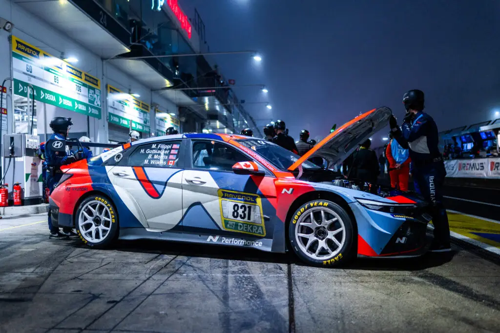 Auto de carreras en boxes, noche, mecánicos trabajando.