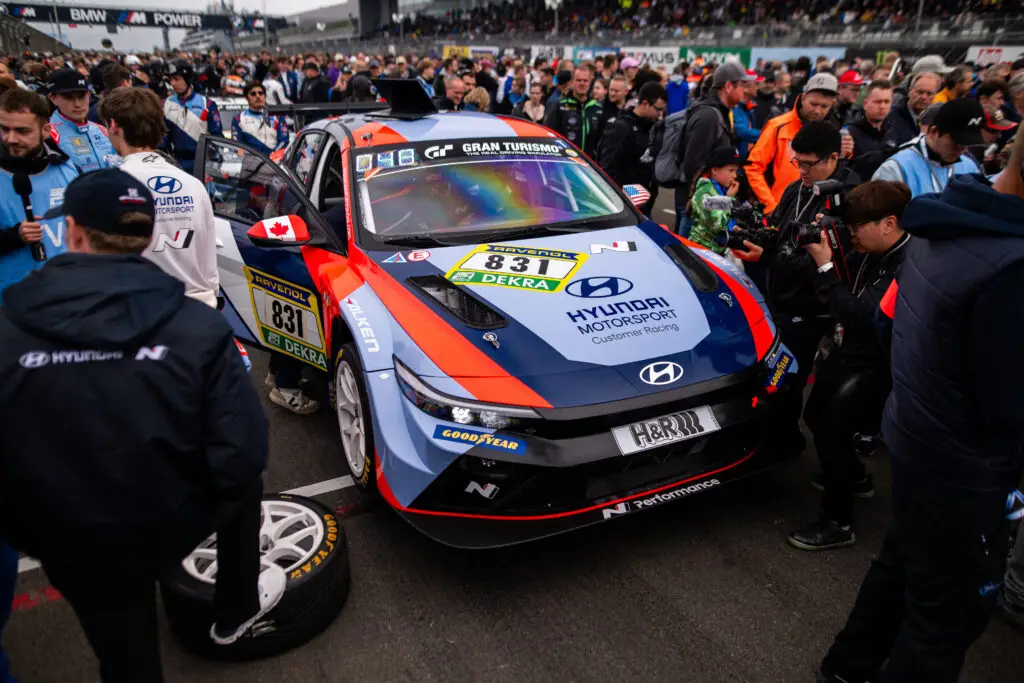 Pilotos y espectadores alrededor de un coche de carreras Hyundai en un evento.