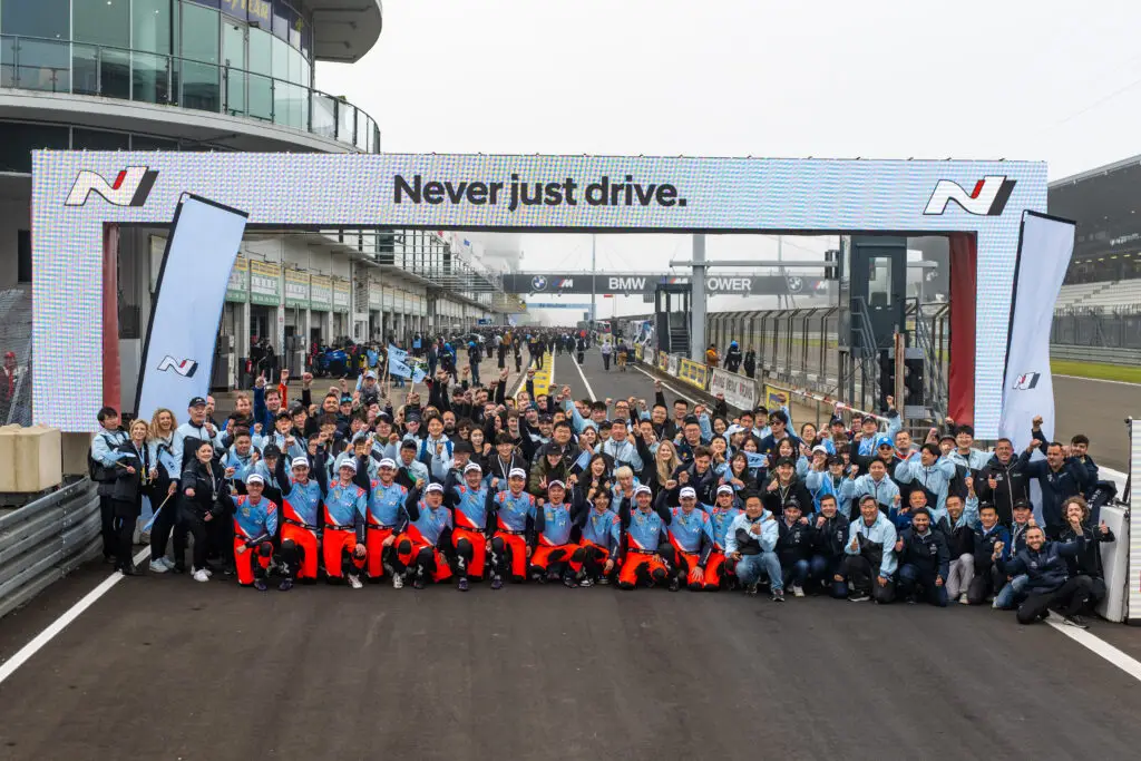 Grupo grande posando en un circuito de carreras, bajo un arco.