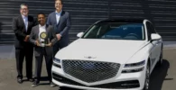 Tres personas en traje con un premio junto a un auto blanco.