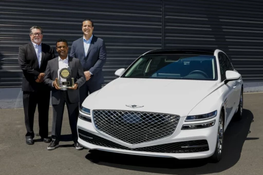 Tres personas en traje con un premio junto a un auto blanco.