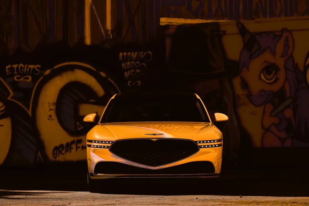 Coche amarillo frente a mural colorido con graffitis.