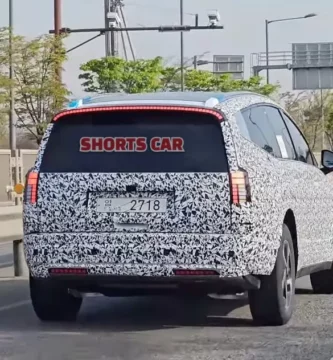 Vehículo camuflado en carretera, con otras, árboles y señales.