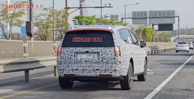 Vehículo camuflado en carretera, con otras, árboles y señales.