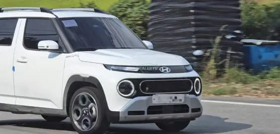 Coche blanco en carretera, matrícula parcialmente borrada.