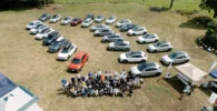 Grupo de personas y muchos autos en una campa.