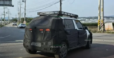 Automóvil camuflado circulando por una carretera con invernaderos a un lado.